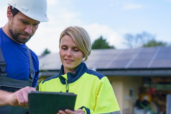 Man and woman solar installers engineers with tablet while installing solar panel system on house.